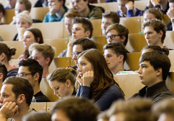 Hörsaal Studierende im Hösraal, Junge Frau im Fokus, die den Kopf auf beide Arme stüzt