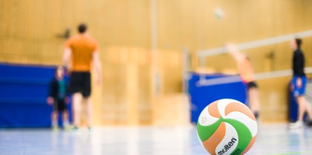 Gym with a volleyball in the front and people playing volleyball in the background