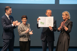Vier Personen stehen auf einer Bühne. Ein Mann erhält eine Urkunde.