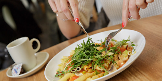 a woman eating a pasta dish in a cafeteria
