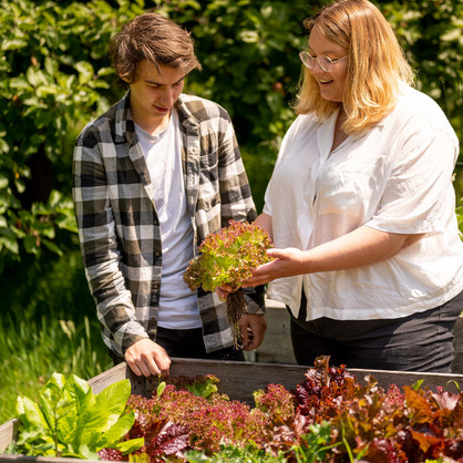 Two young people standing in front of a raised bed with lettuce and holding a picked head of lettuce in their hands