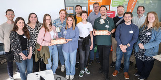 Group photo of 14 people: Some people hold a prize in their hand. Prof. Gerhard Schembecker from TU Dortmund University and Svenja Stepper, Chancellor of Dortmund University of Applied Sciences and Arts, present the Impact Cup to the award winners.